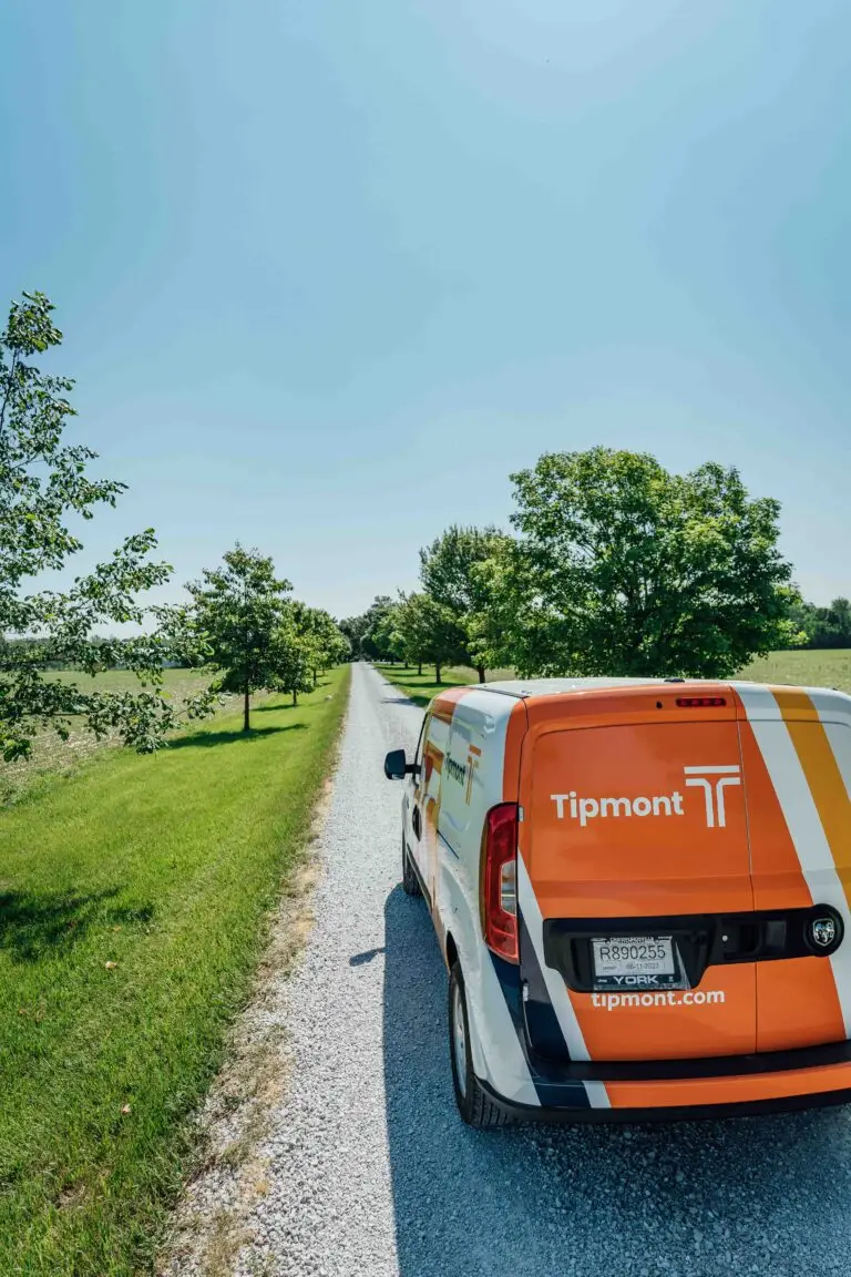 A Tipmont van parked on a rural road on a sunny day with trees in the background