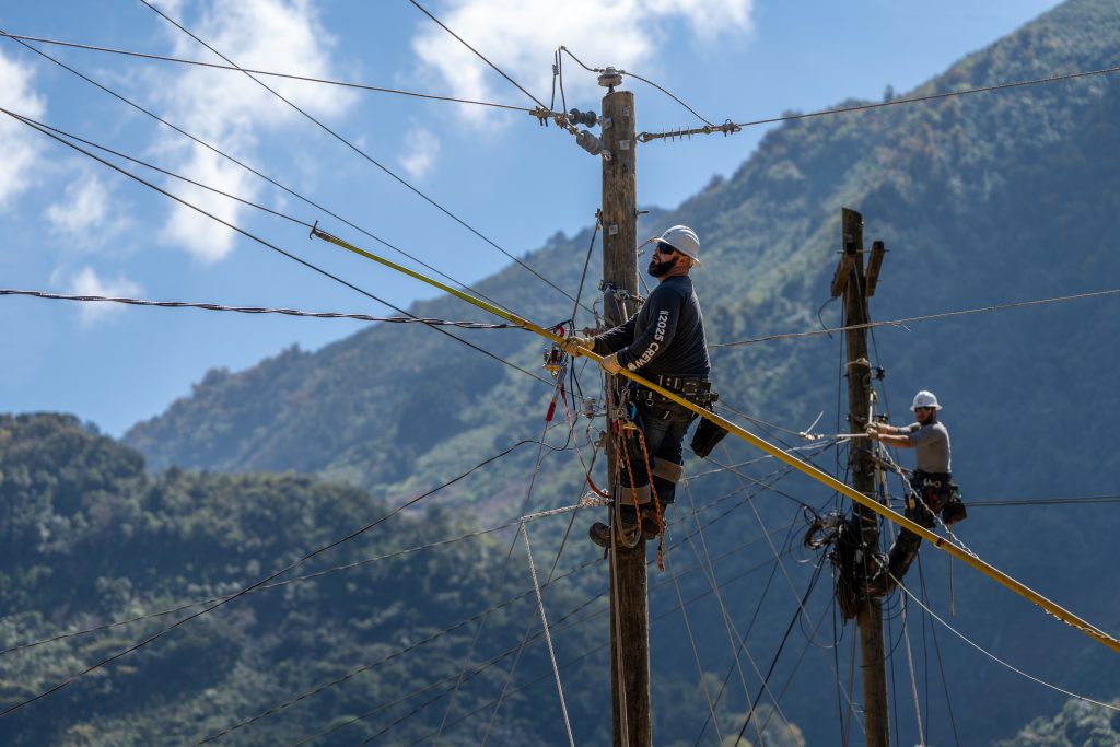Two men working on utility poles near a mountain in Guatemala.