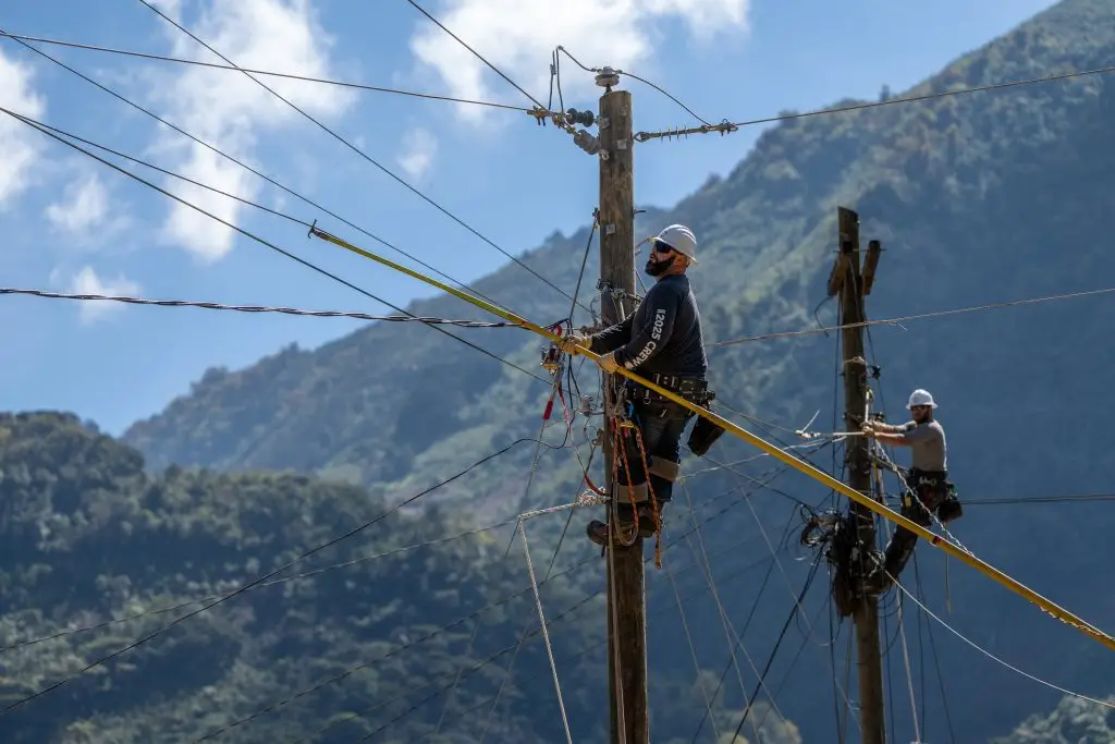 Two men working on utility poles near a mountain in Guatemala.